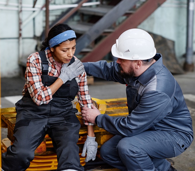 A foreman at a job site giving first aid to a women who has hurt her shoulder.